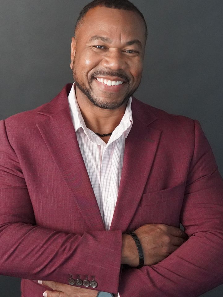 Dee Green smiling with arms crossed in a burgundy blazer